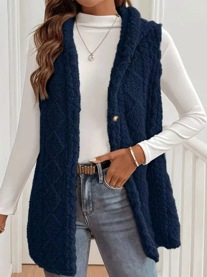 Woman wearing navy blue fuzzy vest over white long-sleeve shirt with jeans and gold accessories