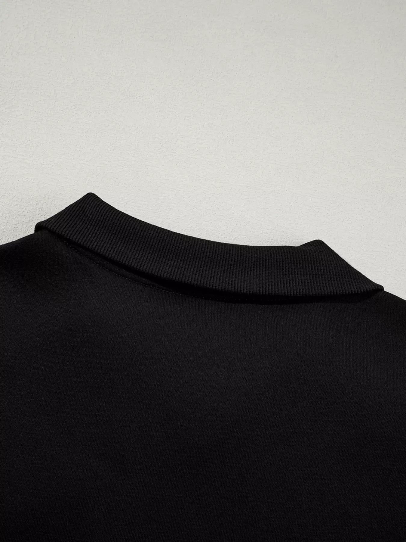 Close-up of black ribbed collar on a black fabric garment against a light textured background