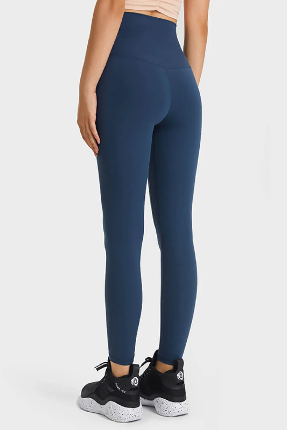 Rear view of woman wearing high-waisted navy blue leggings and black athletic shoes