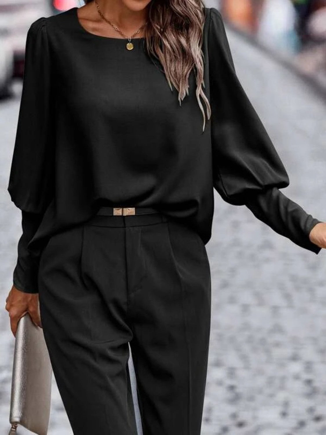Woman wearing chic black blouse with long sleeves and matching tailored black pants