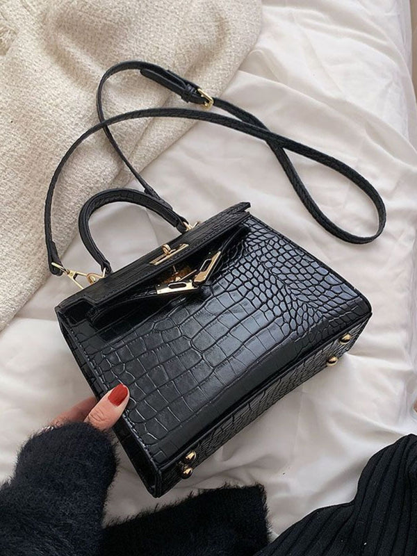 Black crocodile-embossed handbag with gold hardware on a bed, chic women's accessory