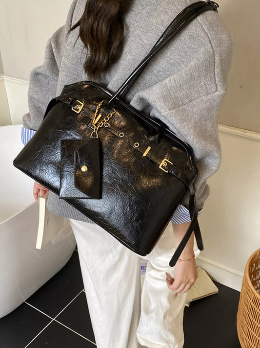 Black textured leather handbag with gold hardware and matching wallet worn by person in gray sweater and white pants