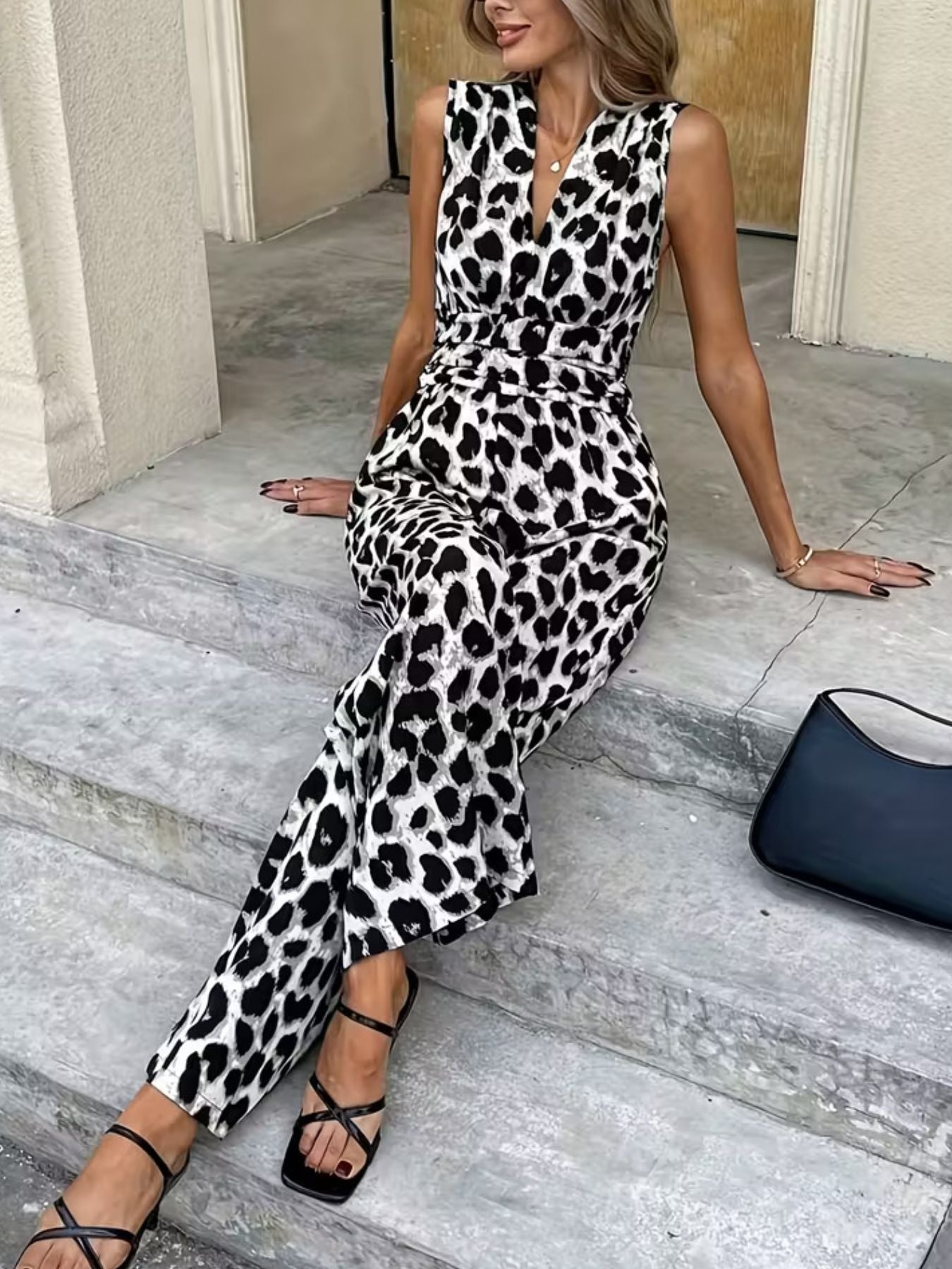 Woman in sleeveless leopard print jumpsuit with black strappy heels and black handbag