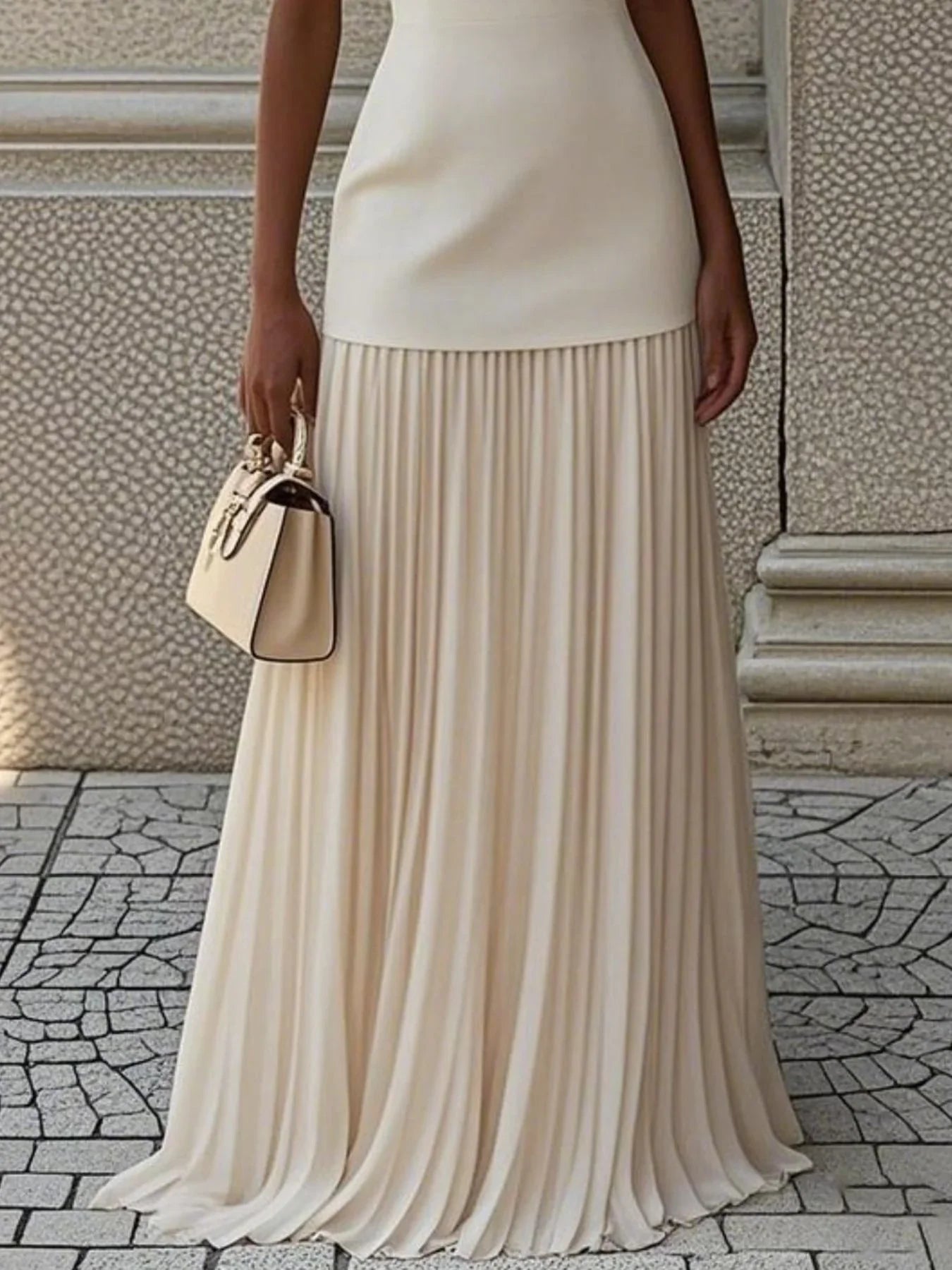 Woman in elegant cream pleated maxi skirt holding a beige handbag outdoors
