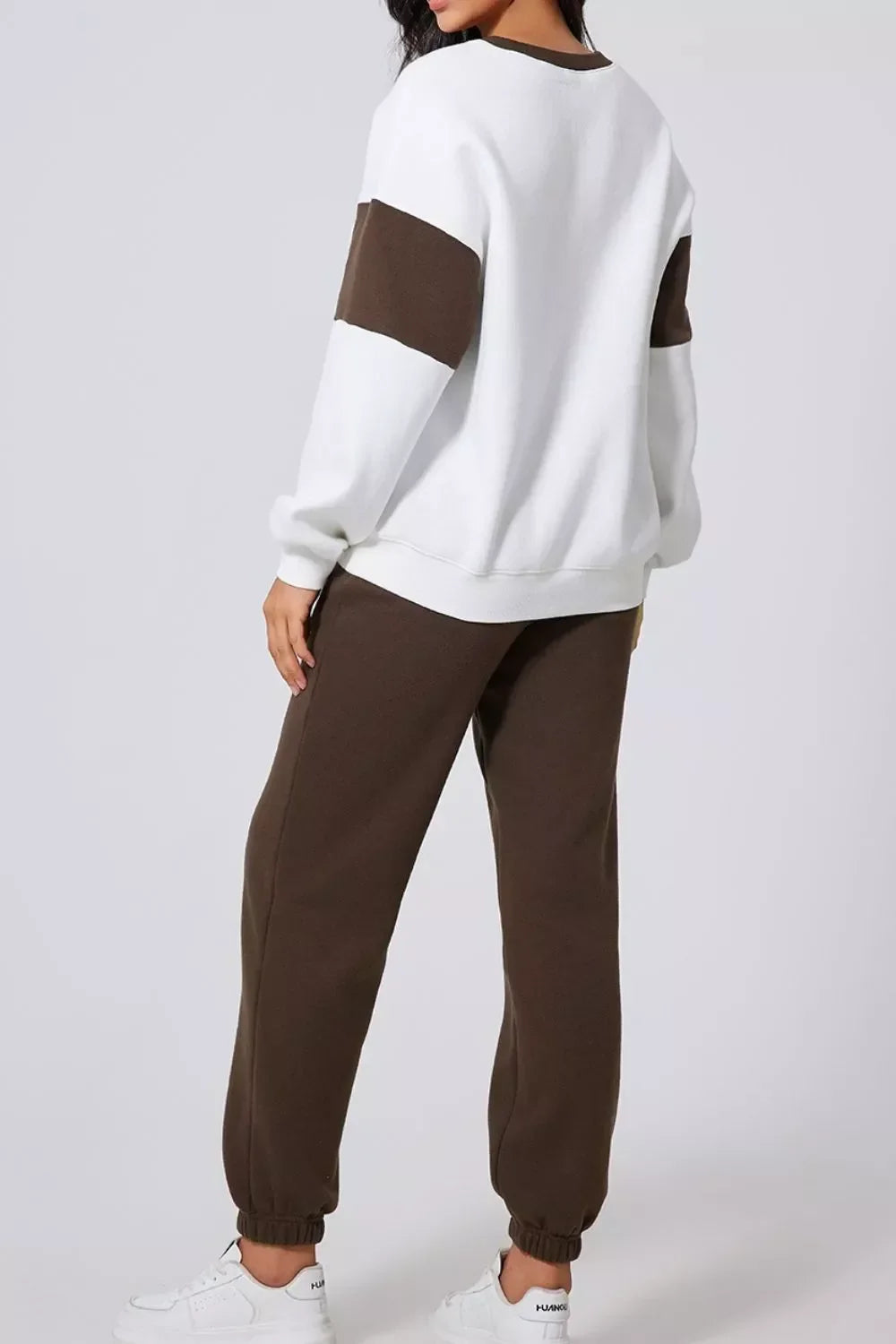 Woman wearing white sweatshirt with brown sleeve panels and brown jogger pants with elastic cuffs