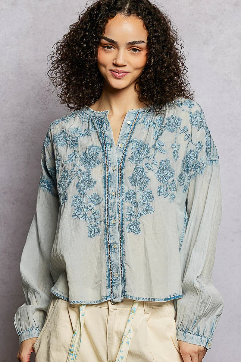 Woman wearing a light blue embroidered floral blouse with long sleeves and cream pants
