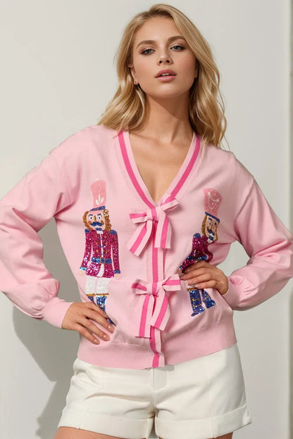Blonde woman wearing pink cardigan with sequined nutcracker designs and white shorts