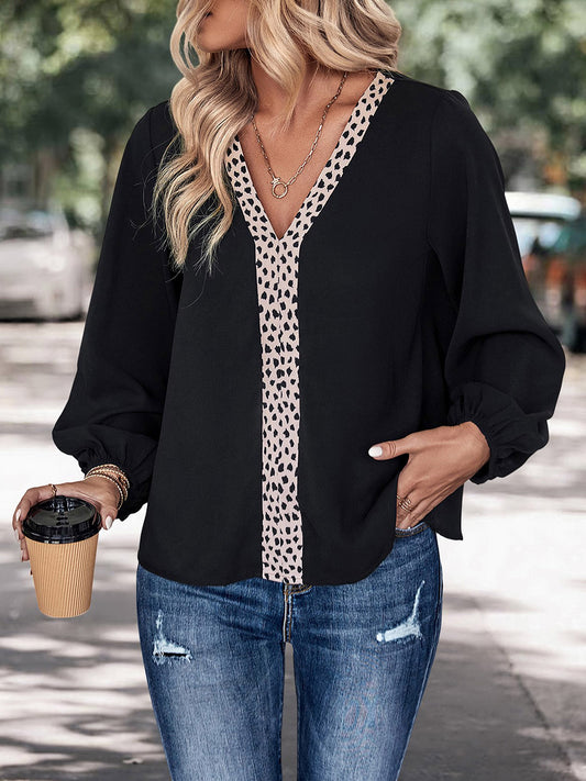Woman wearing black blouse with leopard print V-neck trim and distressed blue jeans holding coffee cup