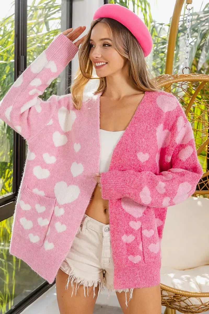 Smiling woman wearing a pink heart-patterned cardigan, white crop top, beige shorts, and pink beret in bright indoor setting