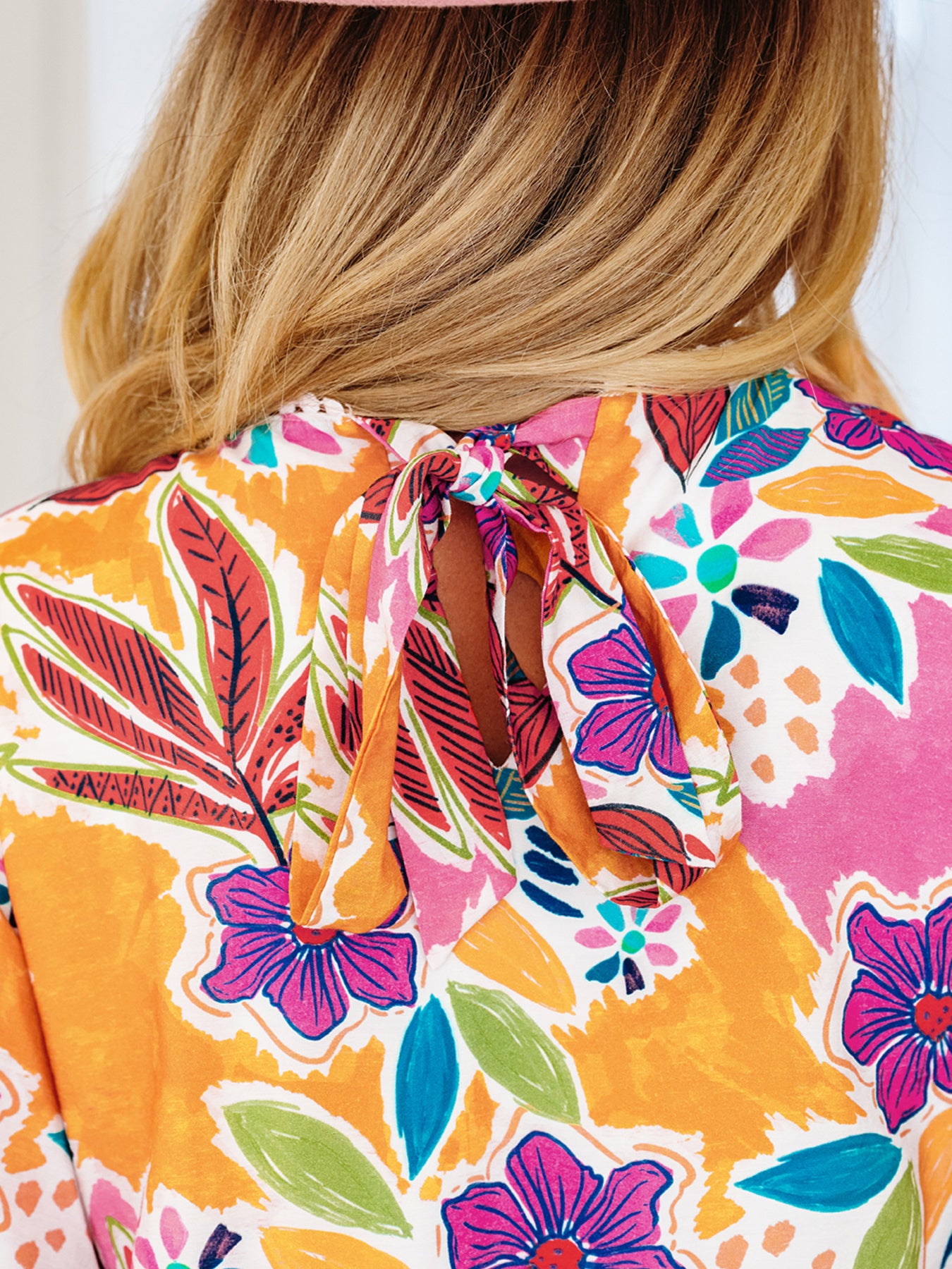 Back view of a woman wearing a vibrant floral blouse with a bow tie neckline