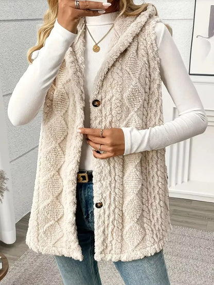 Woman wearing a beige textured faux fur vest over a white long sleeve top with jeans indoors