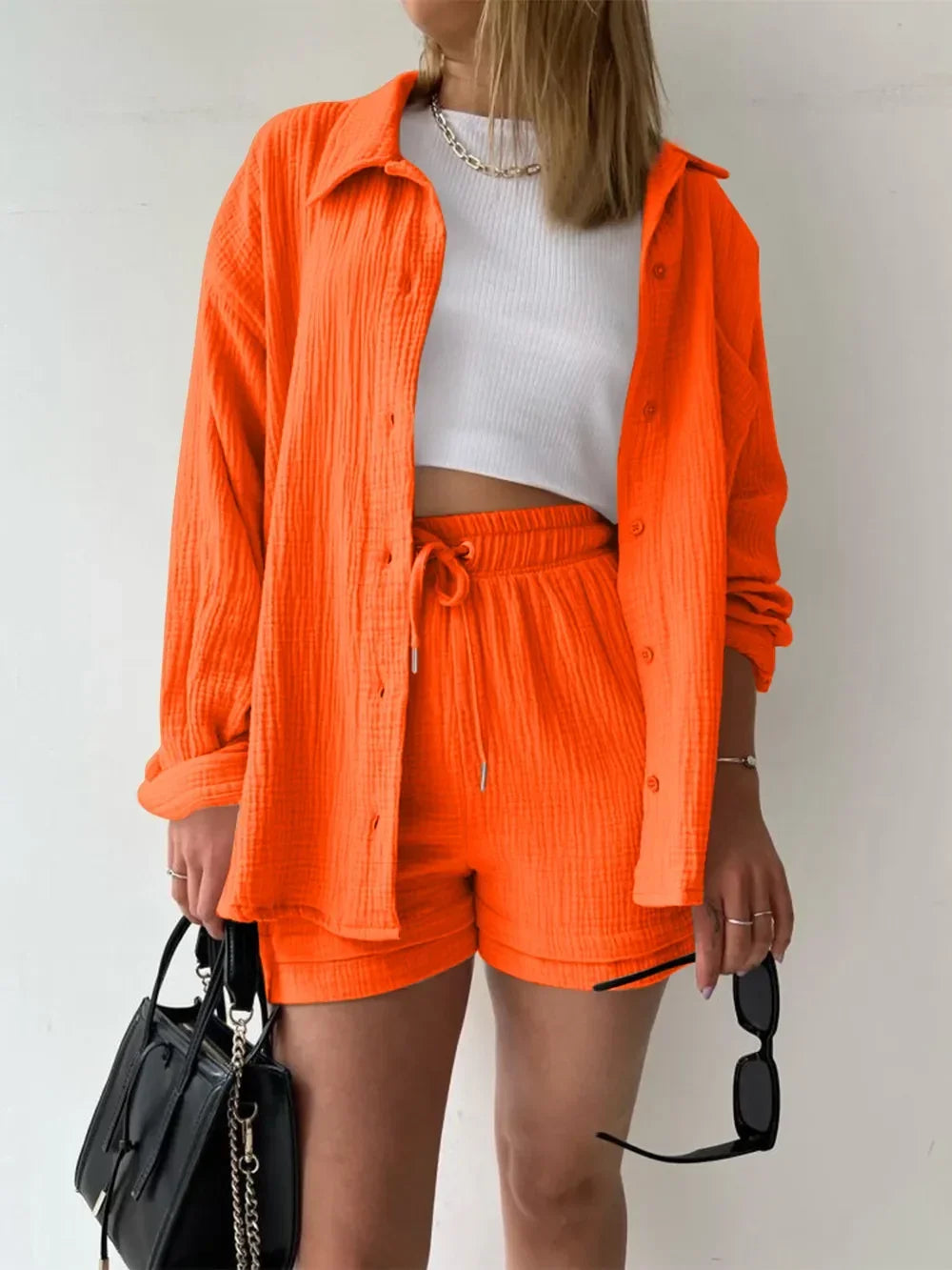 Woman in orange matching shirt and shorts set, white crop top, holding black handbag