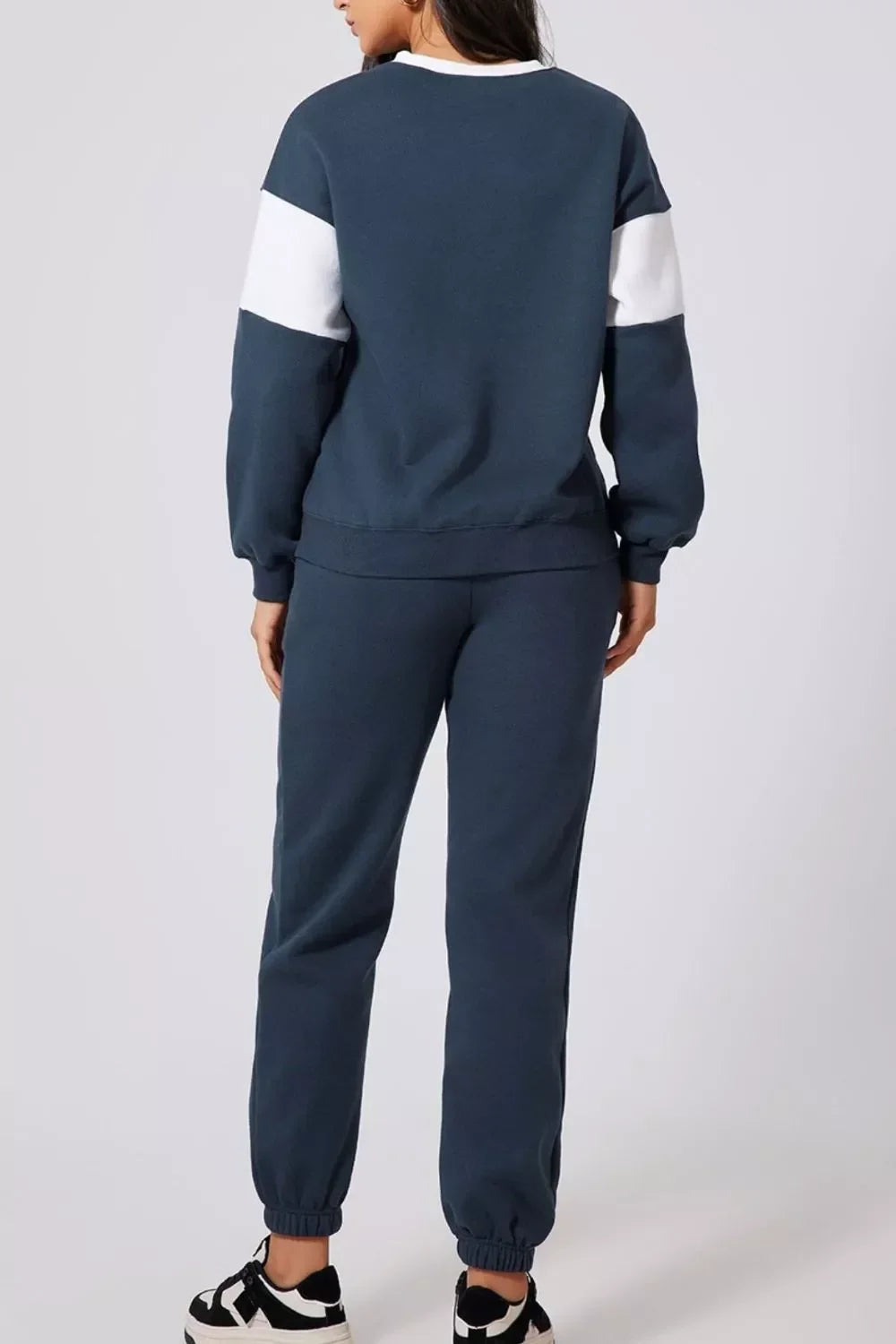 Woman wearing navy blue jogger pants and sweatshirt with white sleeve stripes, standing back