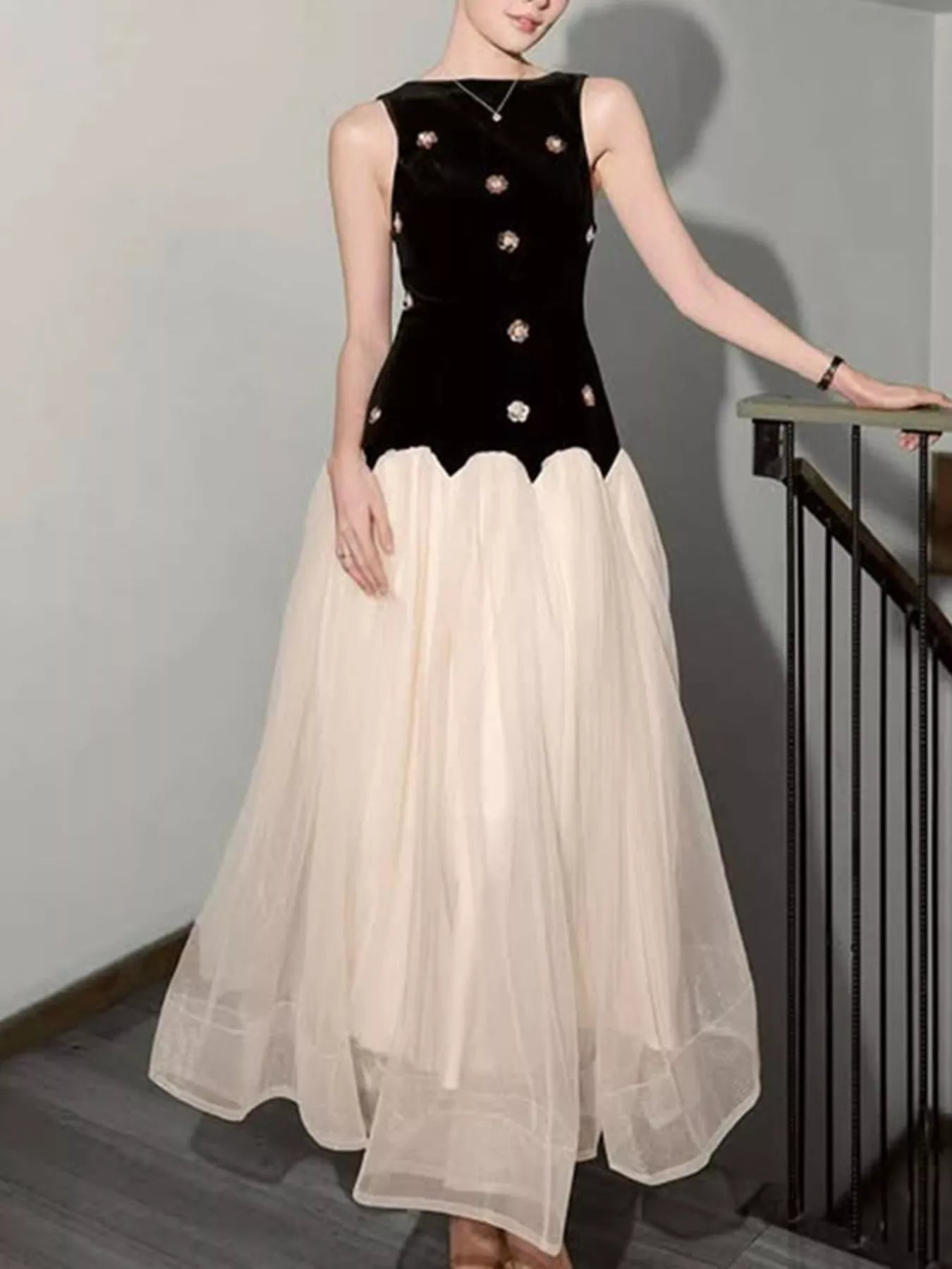 Woman wearing a sleeveless black velvet bodice top with floral embroidery and a flowy cream skirt