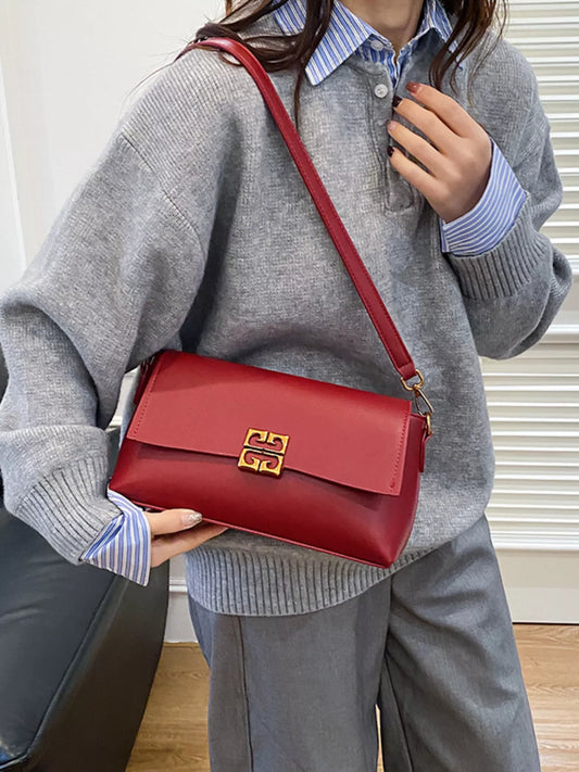 Woman wearing gray sweater and blue striped shirt holding red leather shoulder bag with gold clasp