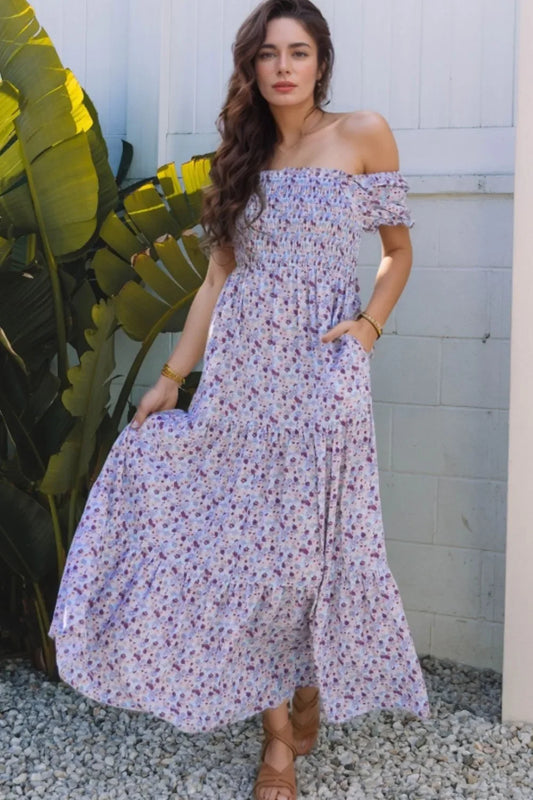 Woman in off-shoulder floral maxi dress posing outdoors by tropical plants