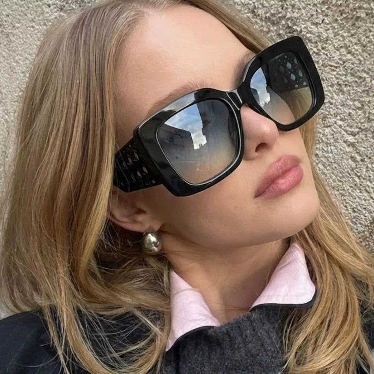 Woman wearing oversized black square sunglasses with cutout temple details.