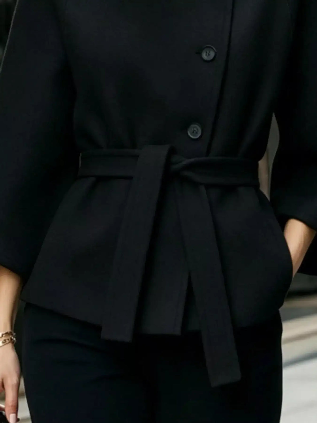 Close-up of a black Evie's Dreamland button-down cape coat with a matching belted waist.