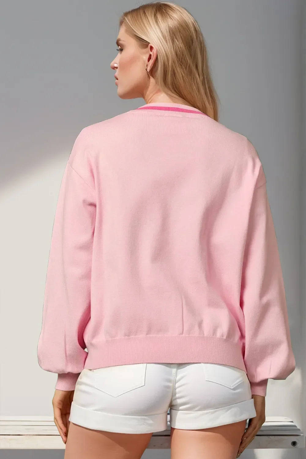 Rear view of woman in light pink sweater and white shorts against neutral background