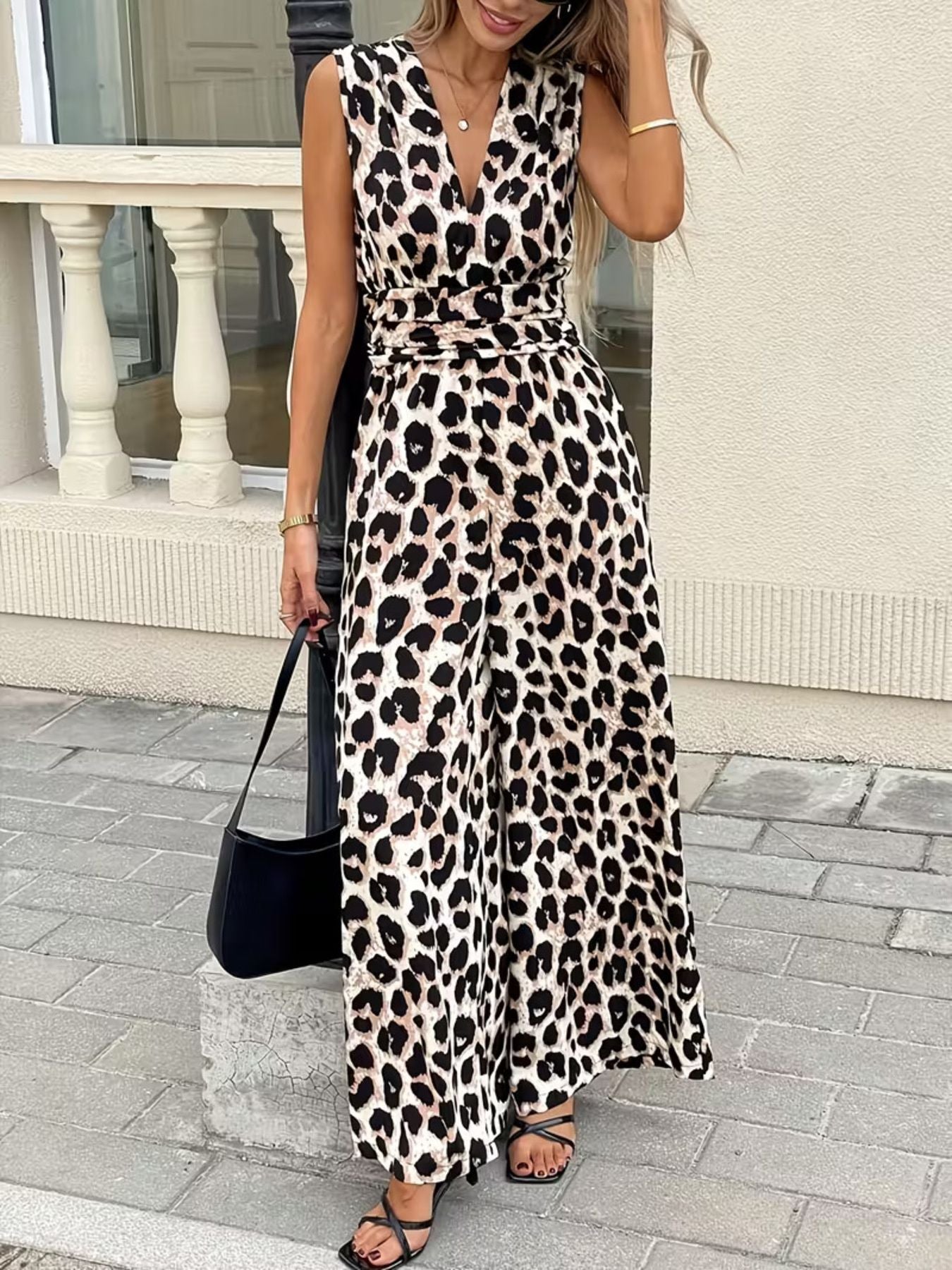 Woman wearing sleeveless leopard print jumpsuit, black sandals, and carrying a black bag