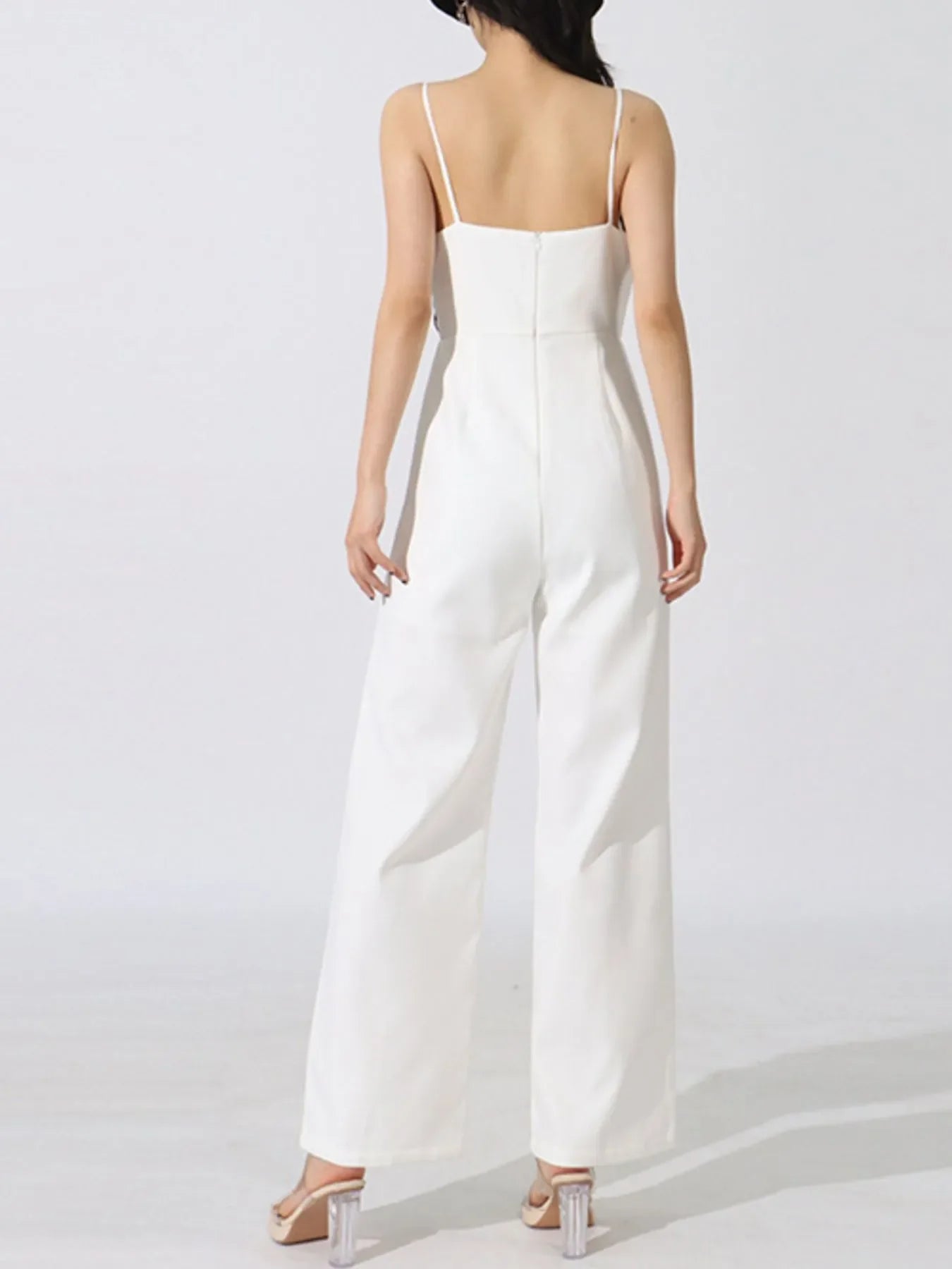 Back view of woman wearing white sleeveless jumpsuit with thin straps and wide leg pants
