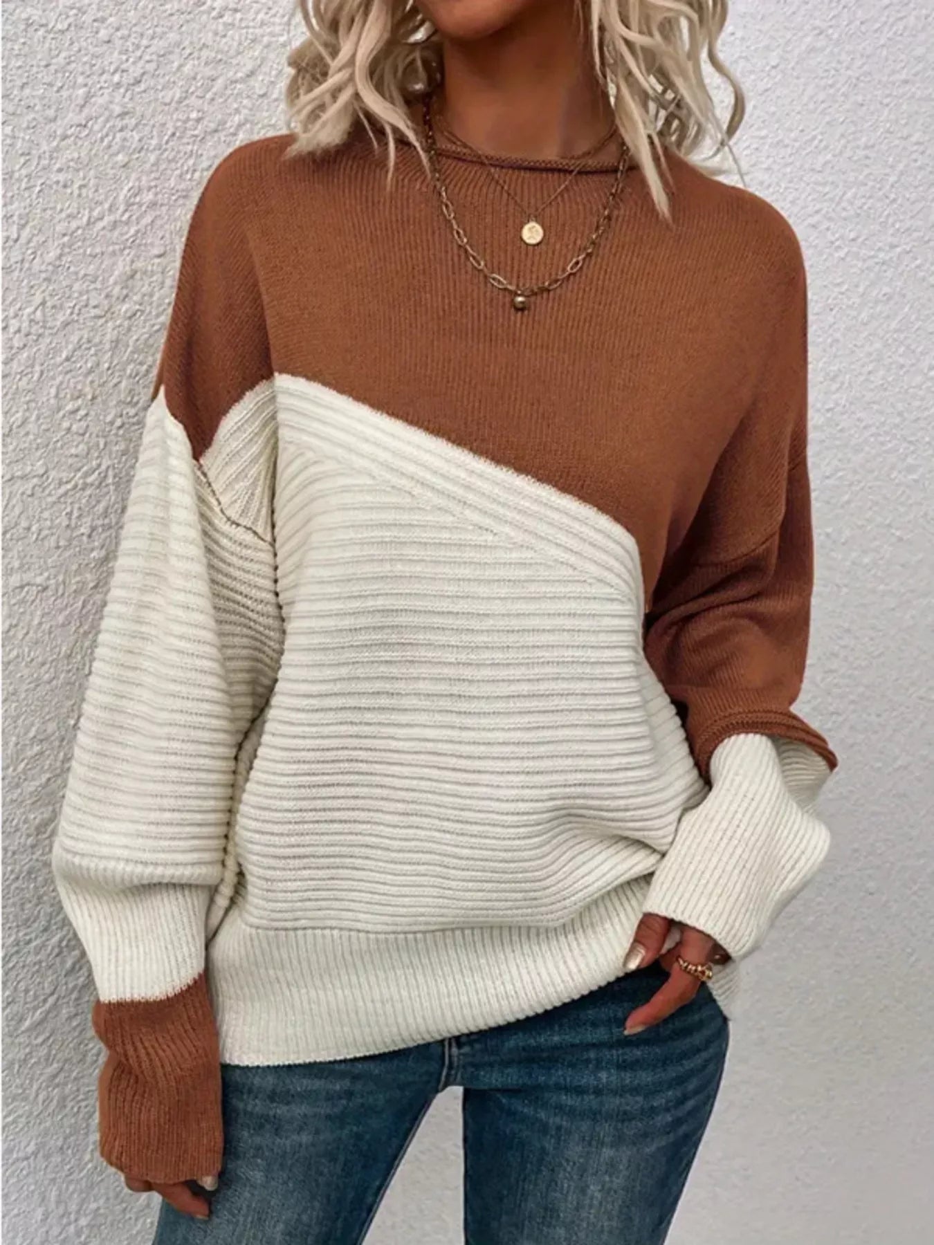 Woman wearing a brown and cream color-block ribbed knit sweater and blue jeans.