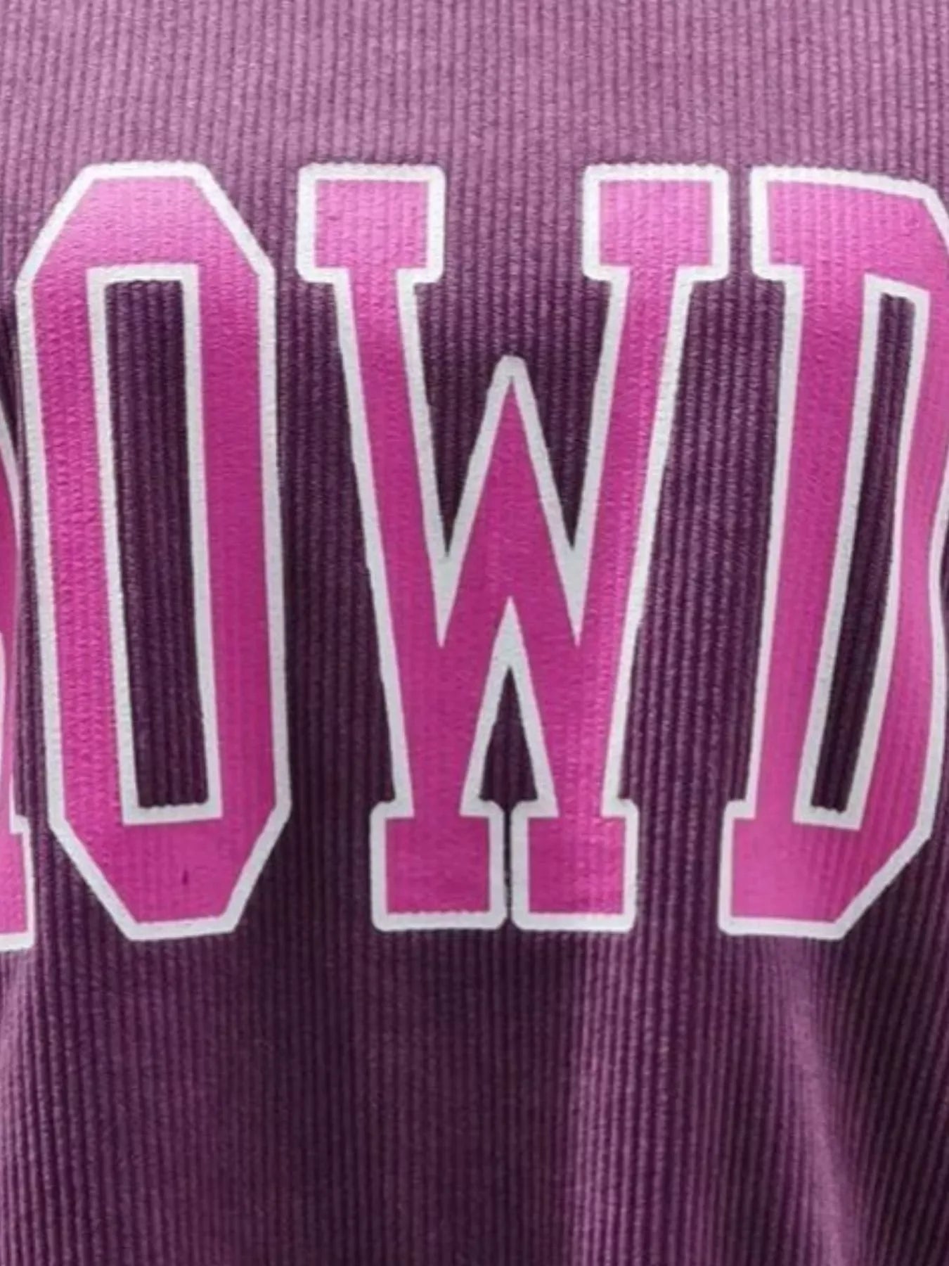 Close-up of purple ribbed fabric with bold pink and white outlined letters spelling part of a word
