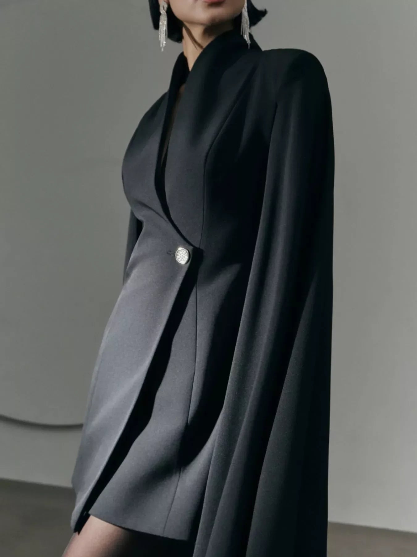 Woman in elegant black blazer dress with single silver button and dangling silver earrings