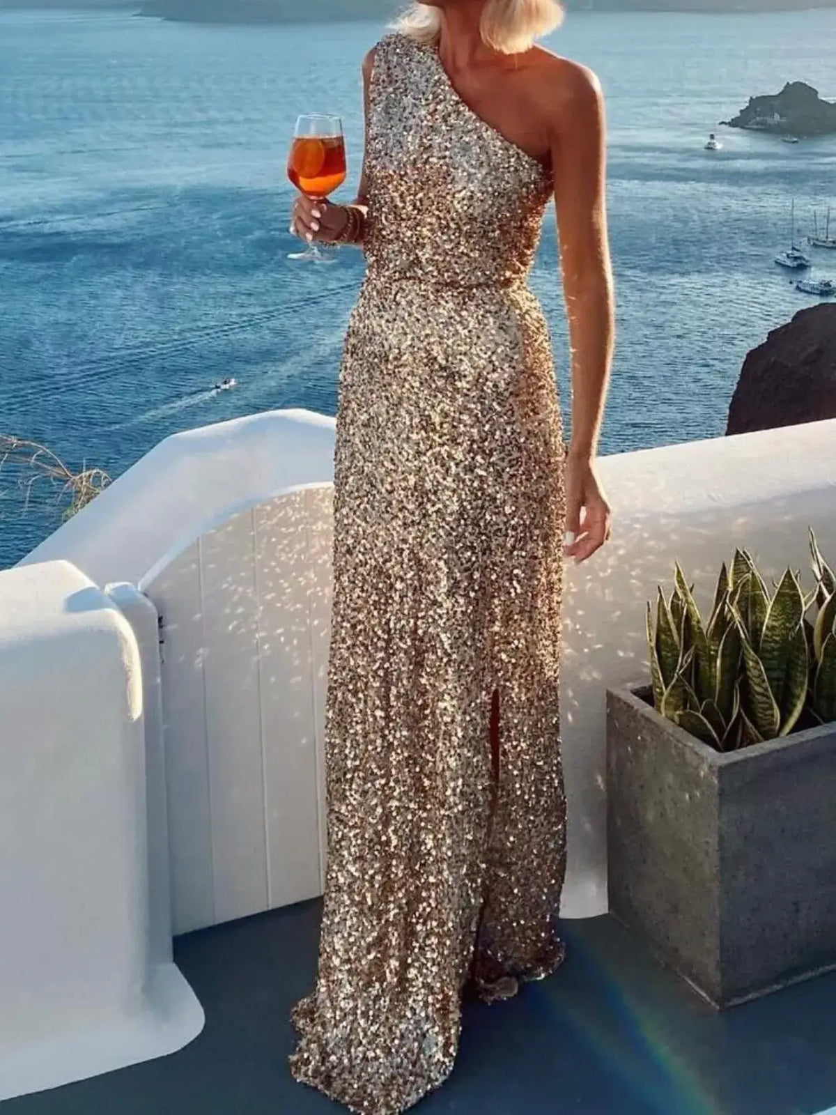 Gold sequin one-shoulder maxi dress with a side slit by Evie's Dreamland, worn by a woman by the sea.