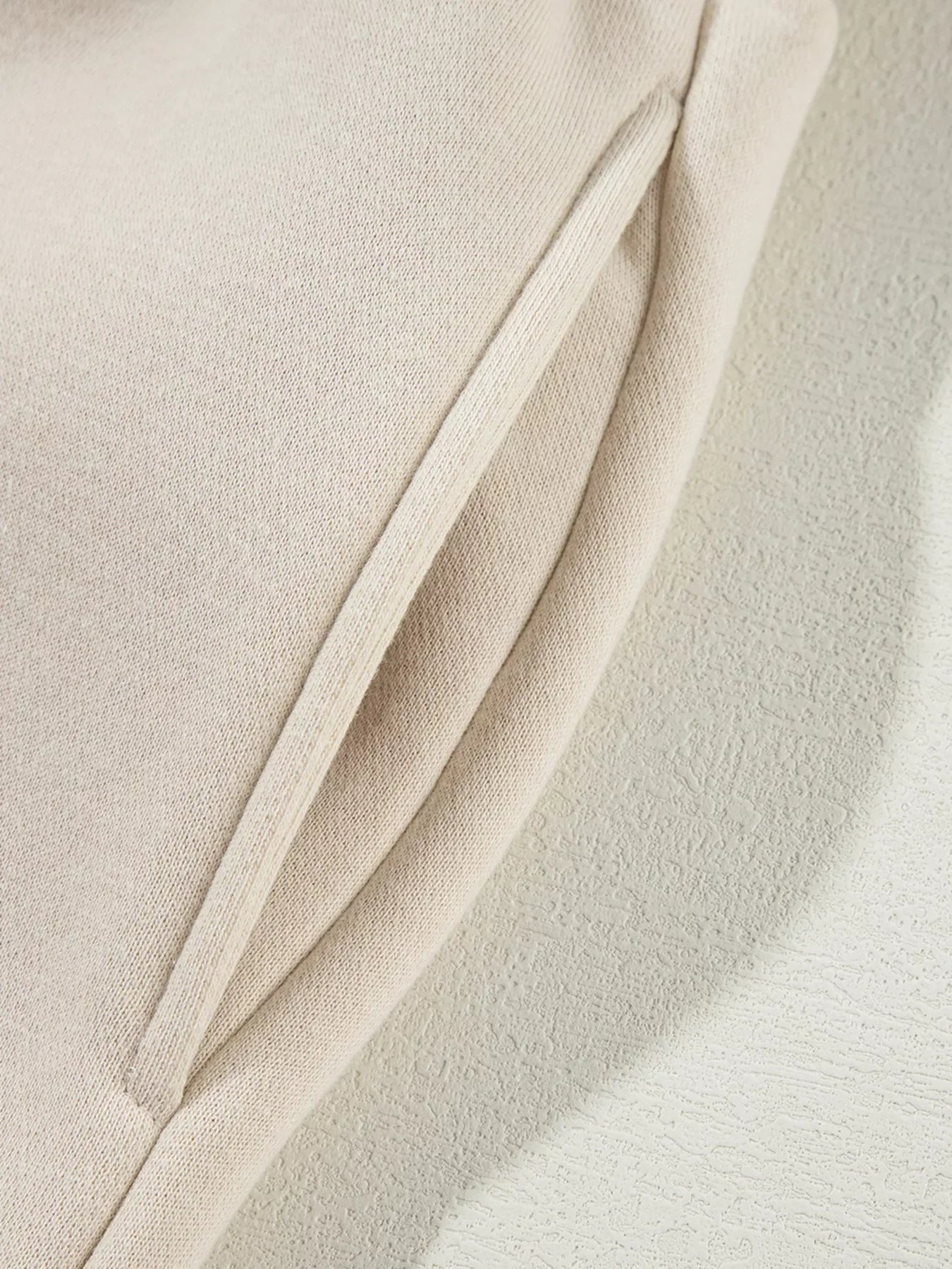 Close-up of beige fabric with a stitched pocket seam on a light textured surface