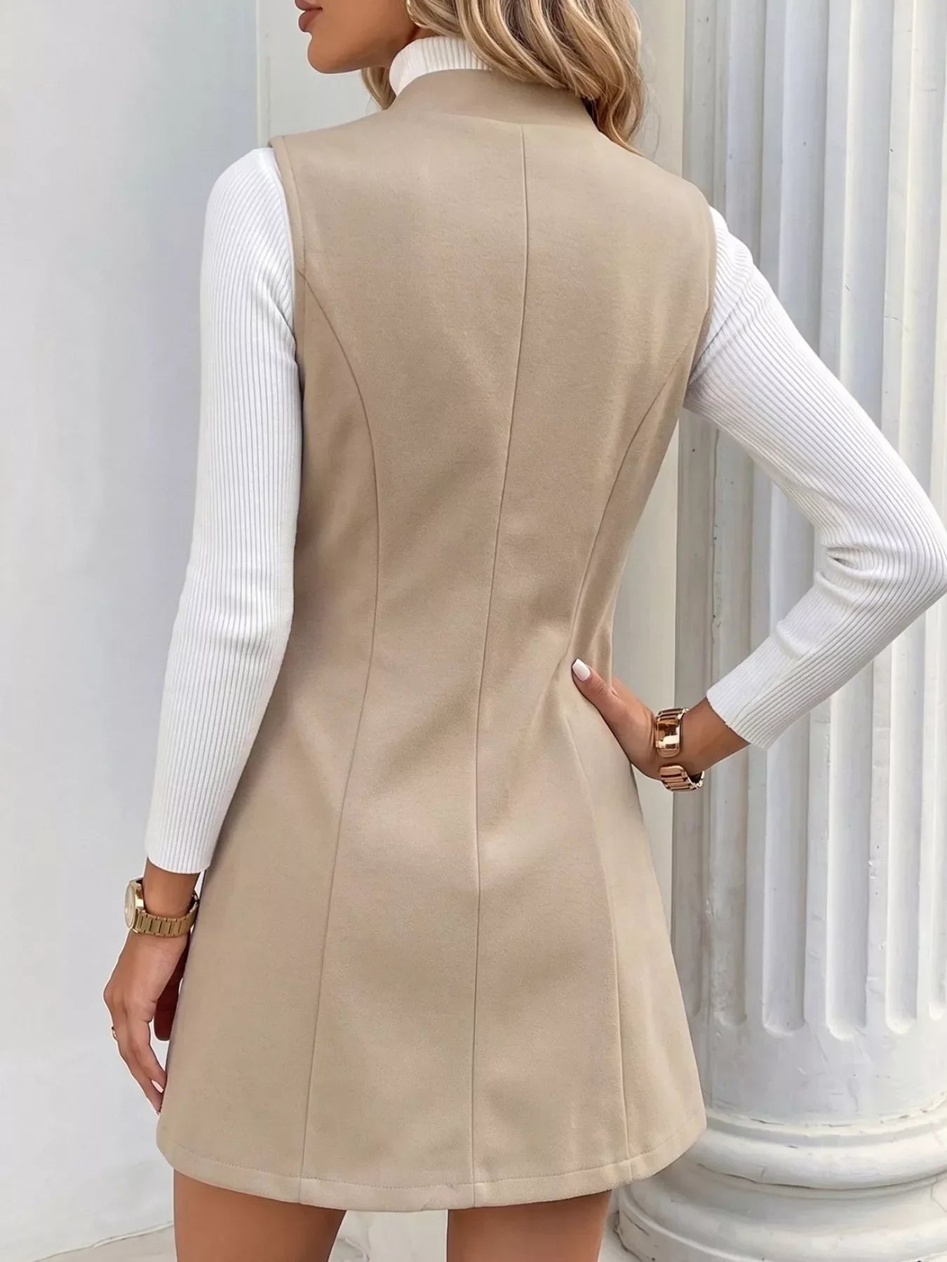 Woman wearing a beige sleeveless dress over a white ribbed turtleneck top