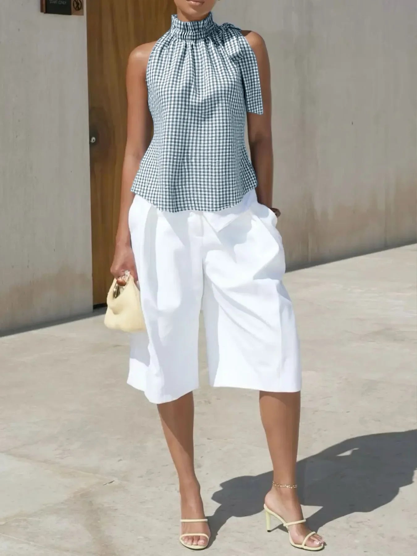 Woman in a sleeveless gingham top and white culotte shorts with heels and handbag