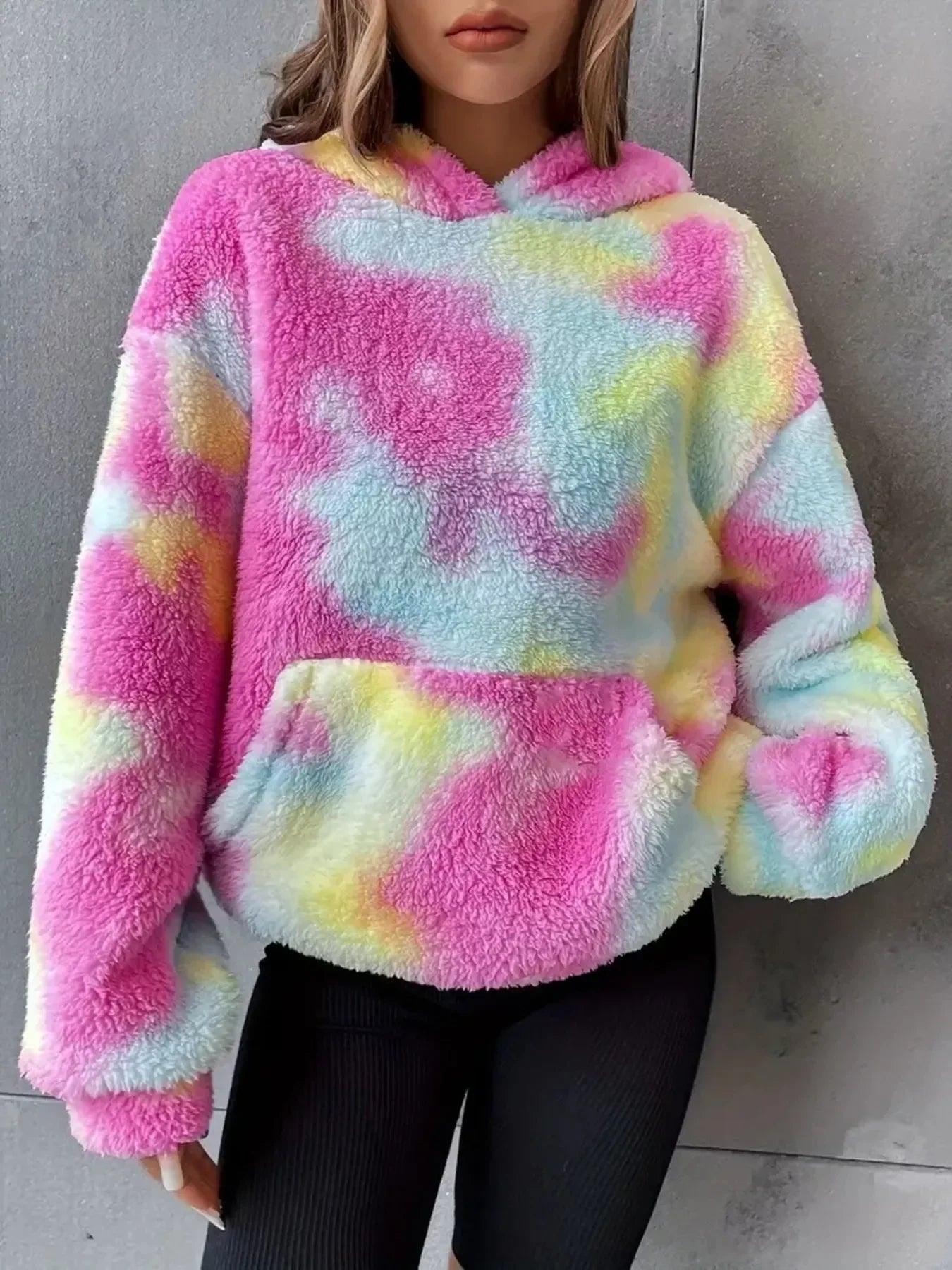 Woman wearing colorful fluffy tie-dye hoodie with pink, blue, and yellow hues against gray wall