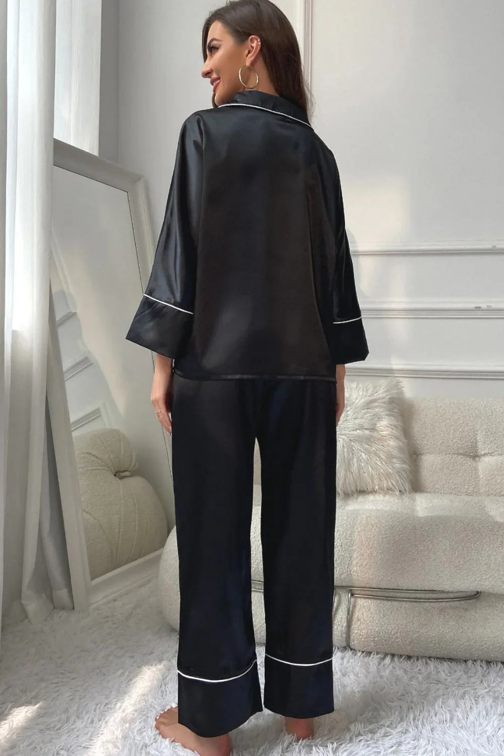 Woman in black silk pajamas with white piping standing barefoot in cozy modern living room