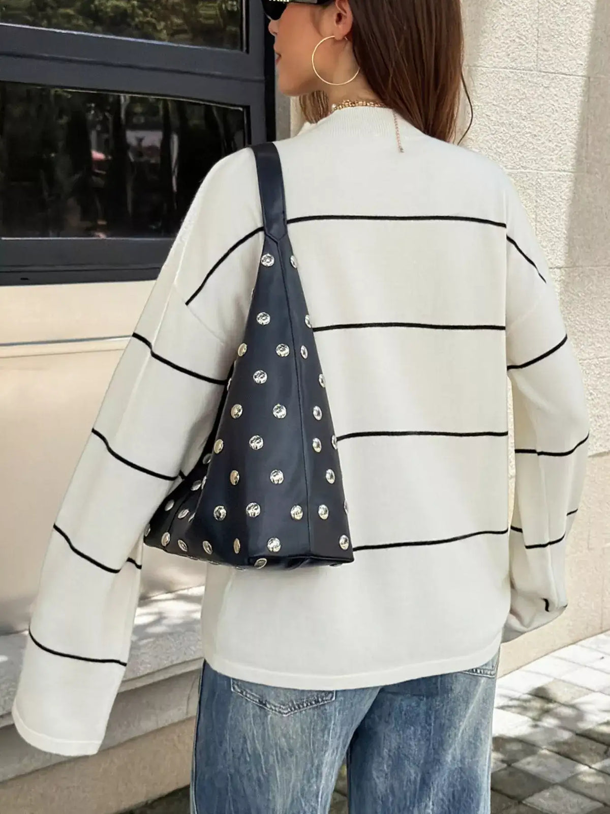 Back view of a white Evie's Dreamland striped mock neck sweater paired with a black studded shoulder bag.