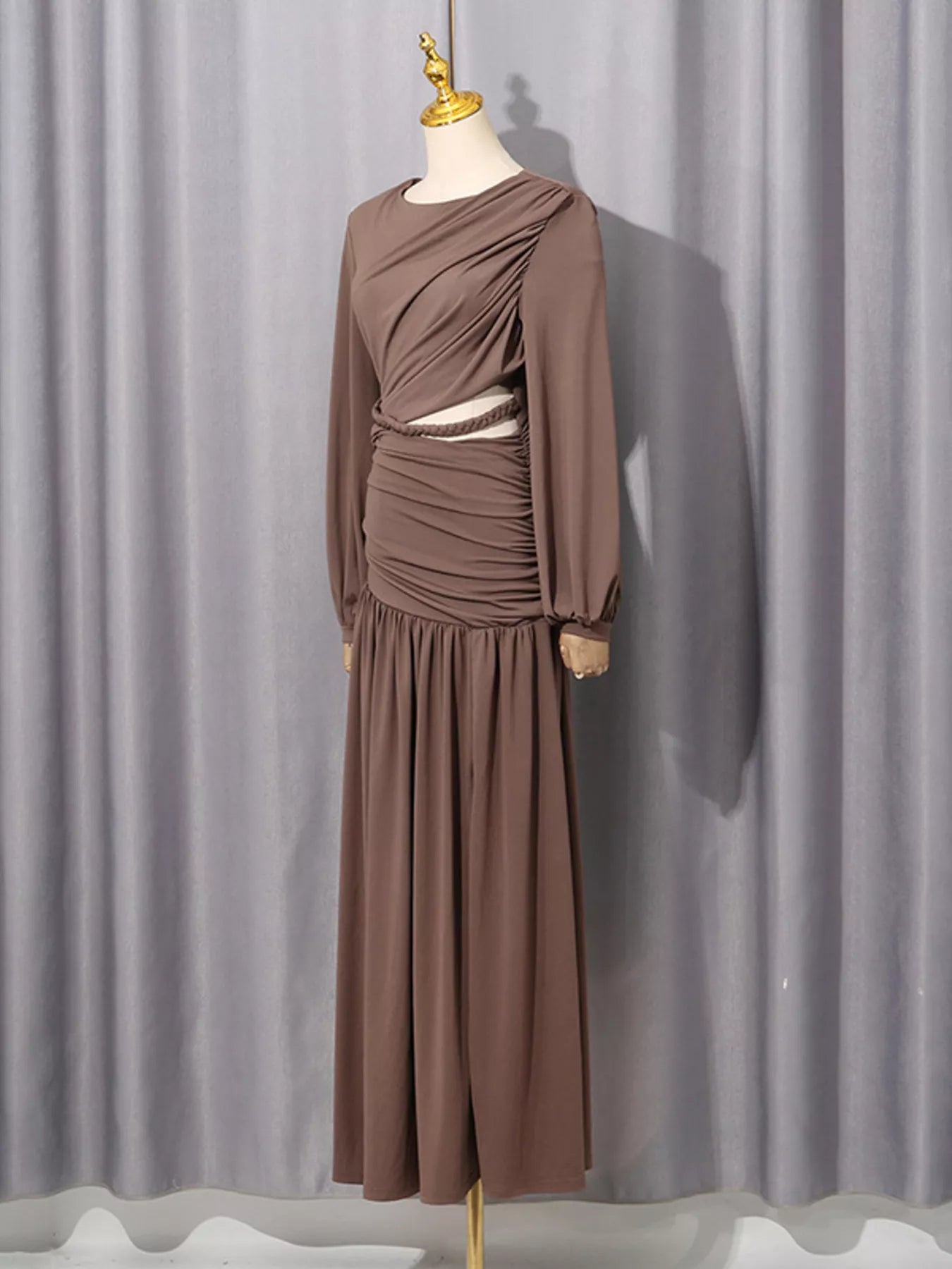 Taupe long-sleeve maxi dress with ruched bodice and waist cutout on a mannequin