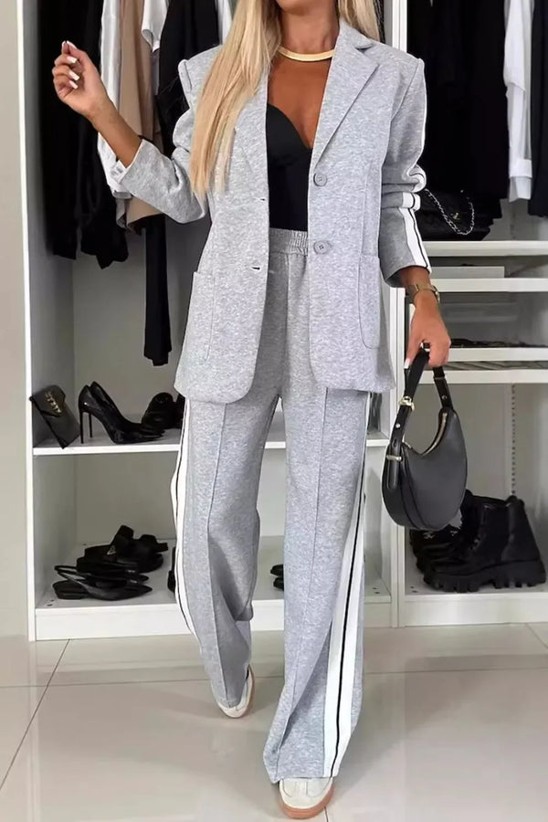 Woman wearing gray casual blazer and wide-leg pants with side stripes, holding black handbag in modern closet
