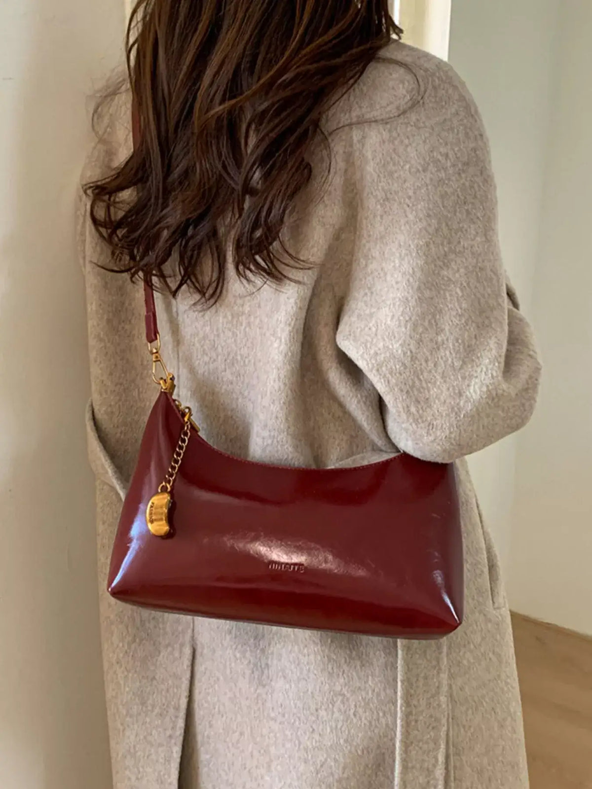 Woman wearing a beige coat and a burgundy PU leather shoulder bag with a gold chain charm.
