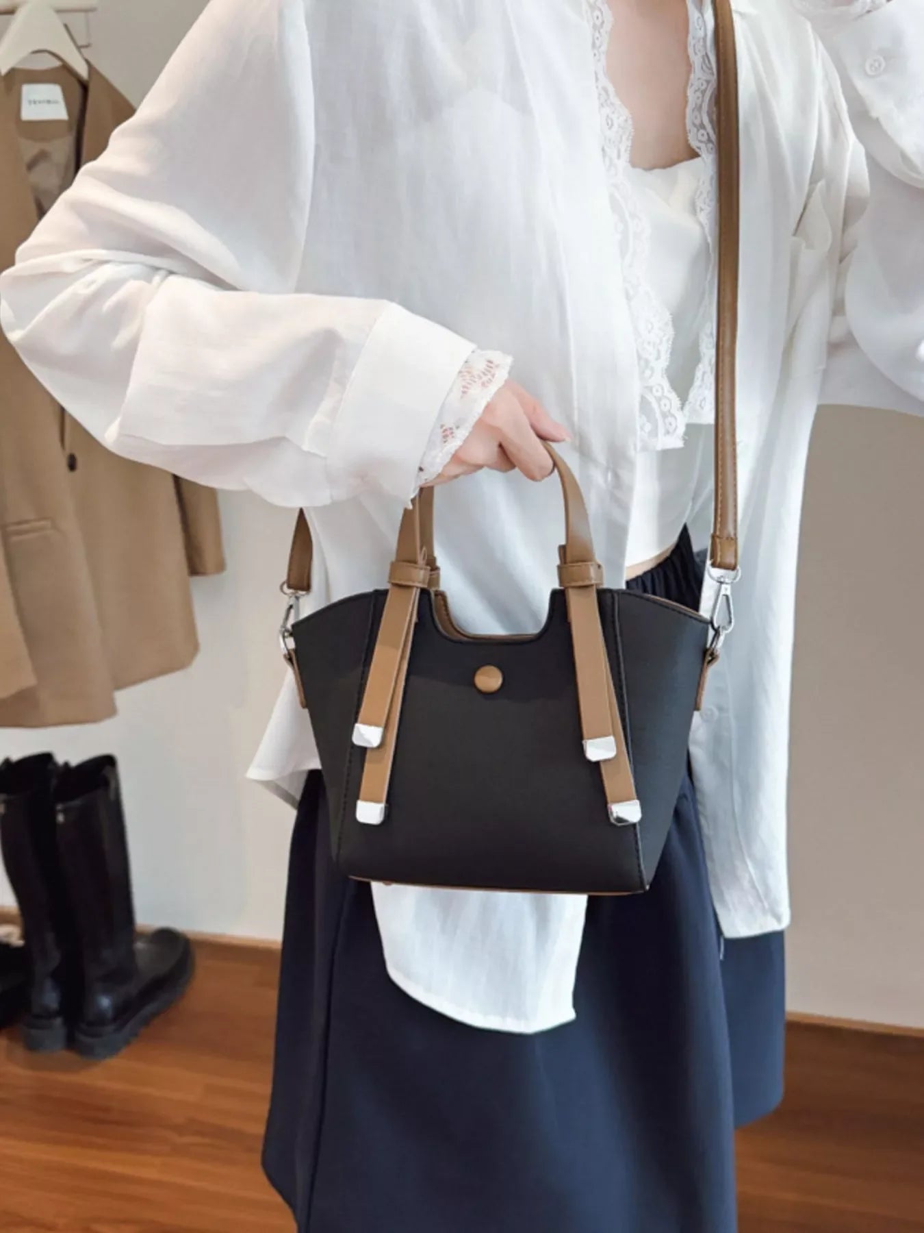 Woman wearing white blouse and dark skirt holding black and brown leather handbag indoors