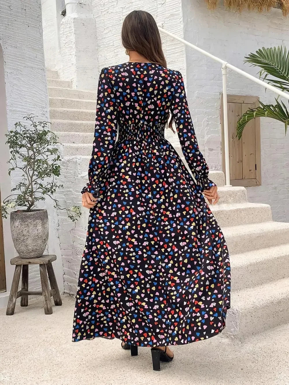 Woman in black long-sleeve maxi dress with colorful heart print walking up white stairs outdoors