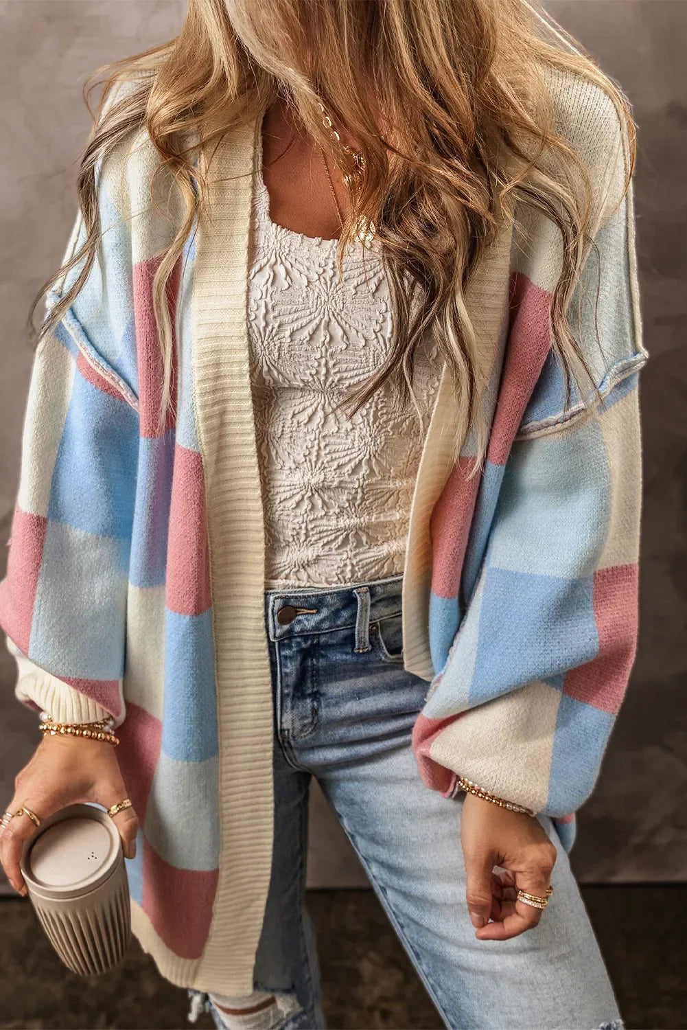 Woman wearing pastel checkered cardigan, white textured top, ripped jeans, holding a cup