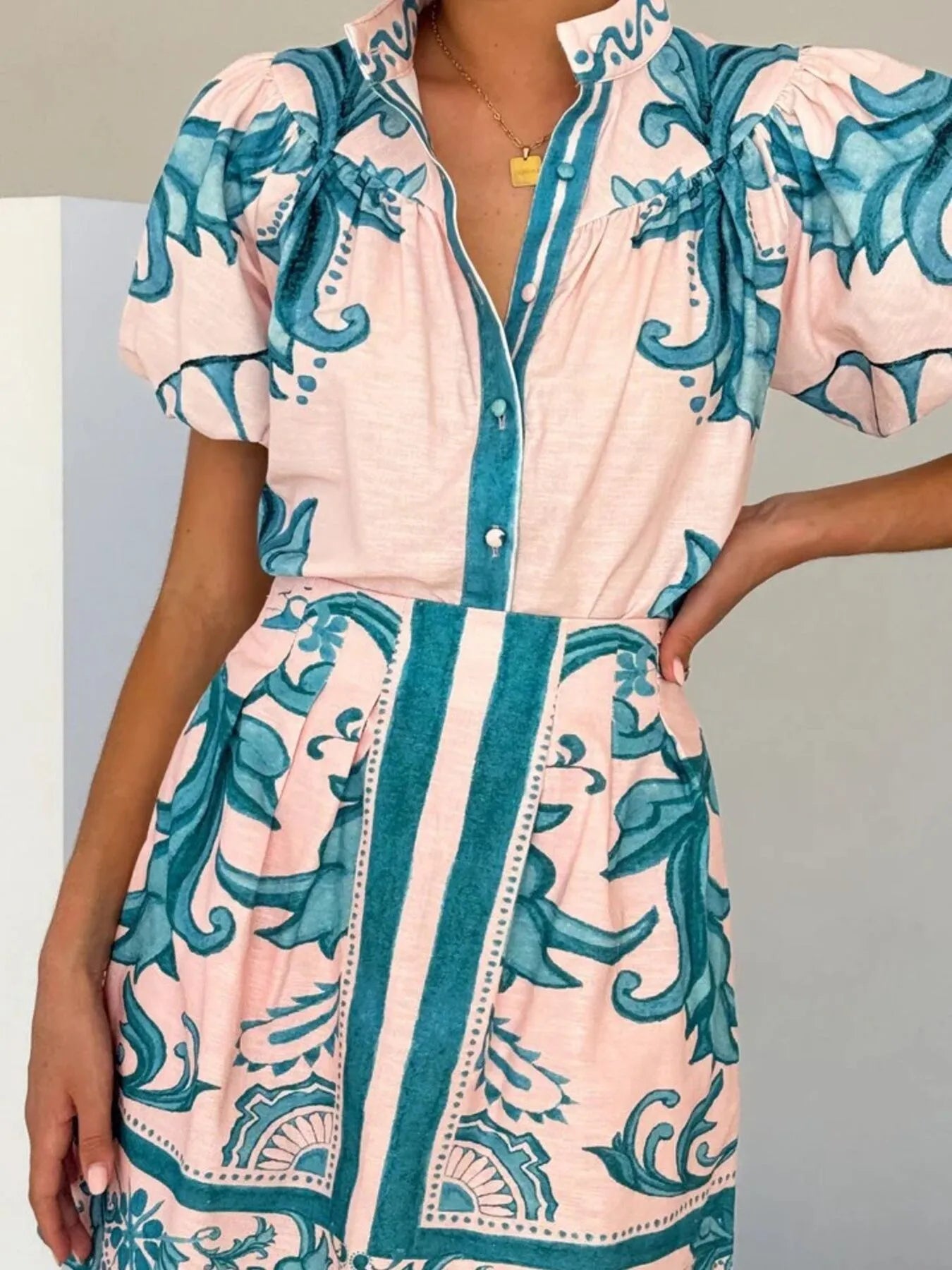 Woman wearing a pink button-front dress with teal floral patterns and puff sleeves