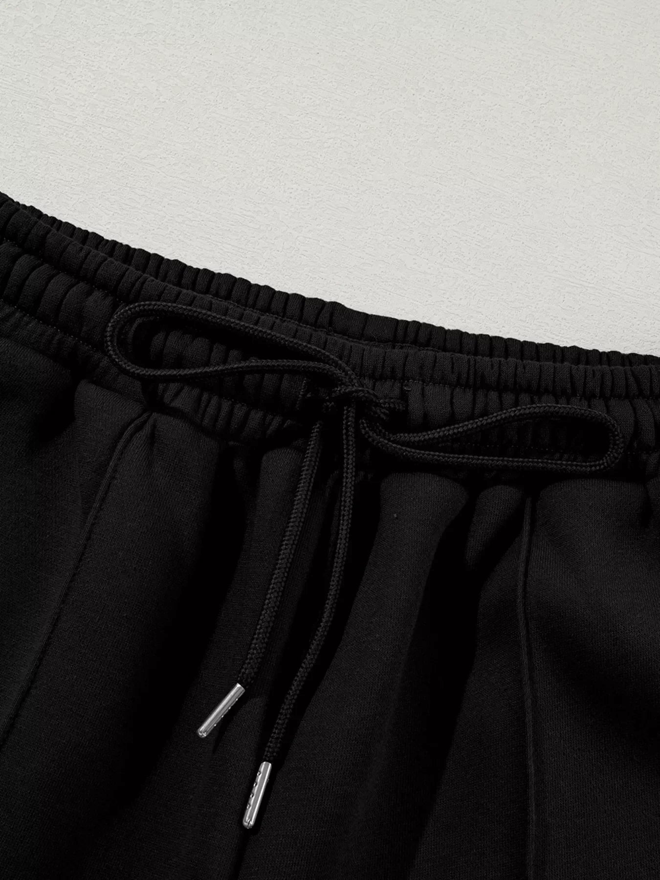 Close-up of black sweatpants waistband with elastic and drawstring on textured gray background