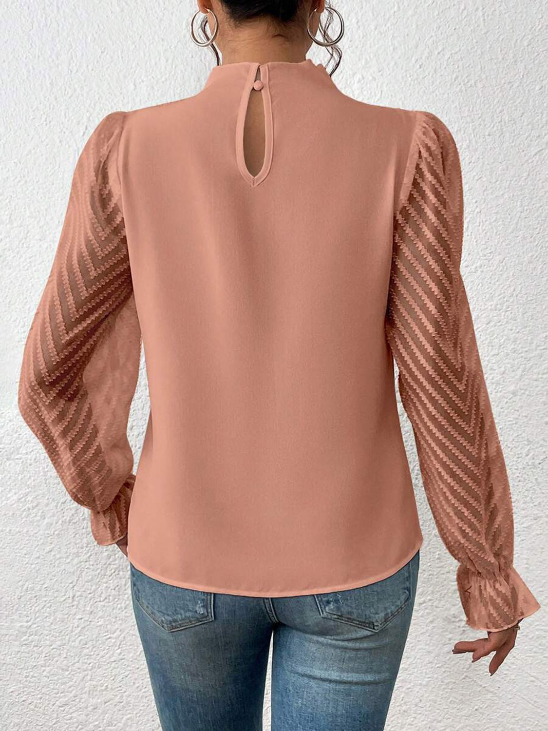 Woman wearing a dusty pink long sleeve blouse with sheer chevron sleeves and jeans, viewed from back