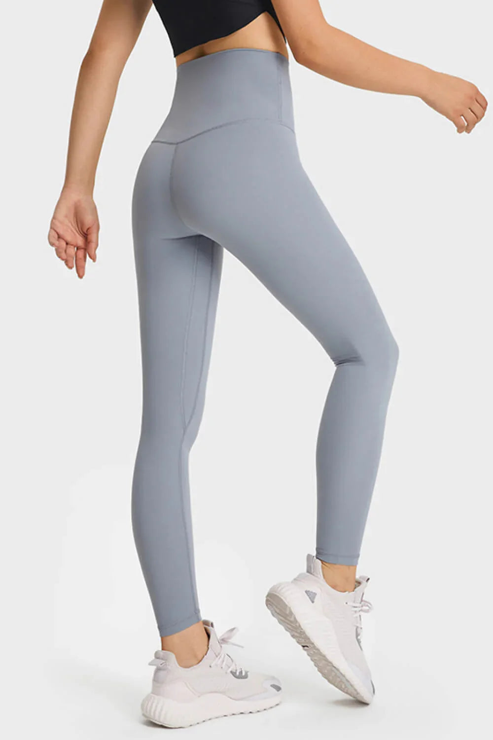 Woman wearing high-waisted light blue leggings and white athletic sneakers, side view