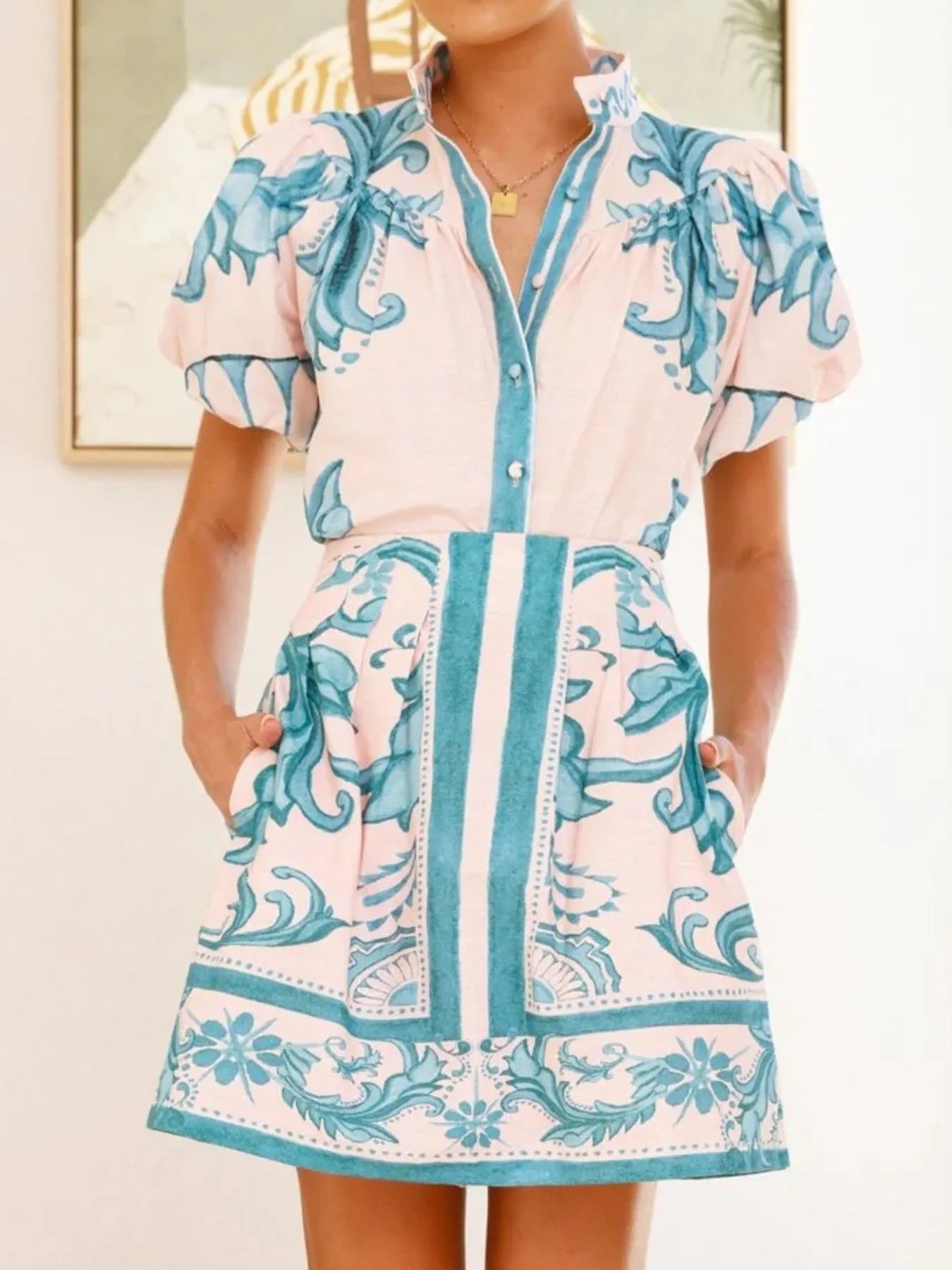 Woman wearing a short pink dress with blue floral print and puff sleeves, standing indoors