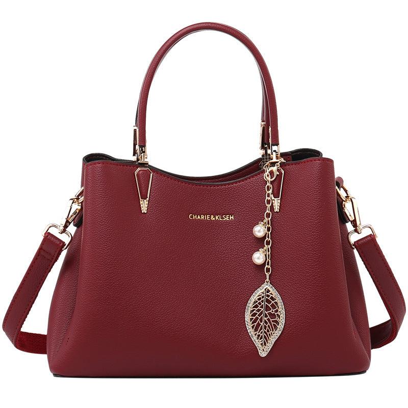 Burgundy leather handbag with gold hardware, top handles, shoulder strap, and leaf charm