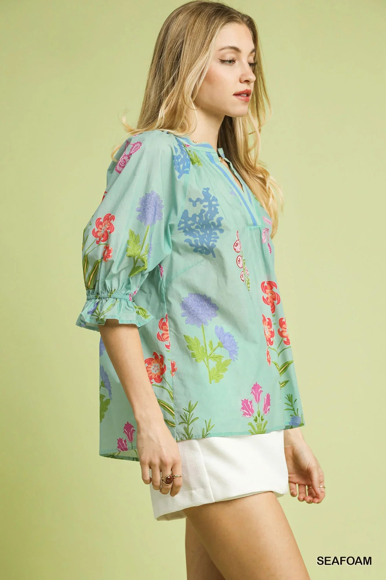 Woman wearing a seafoam green floral blouse with puff sleeves and a white mini skirt