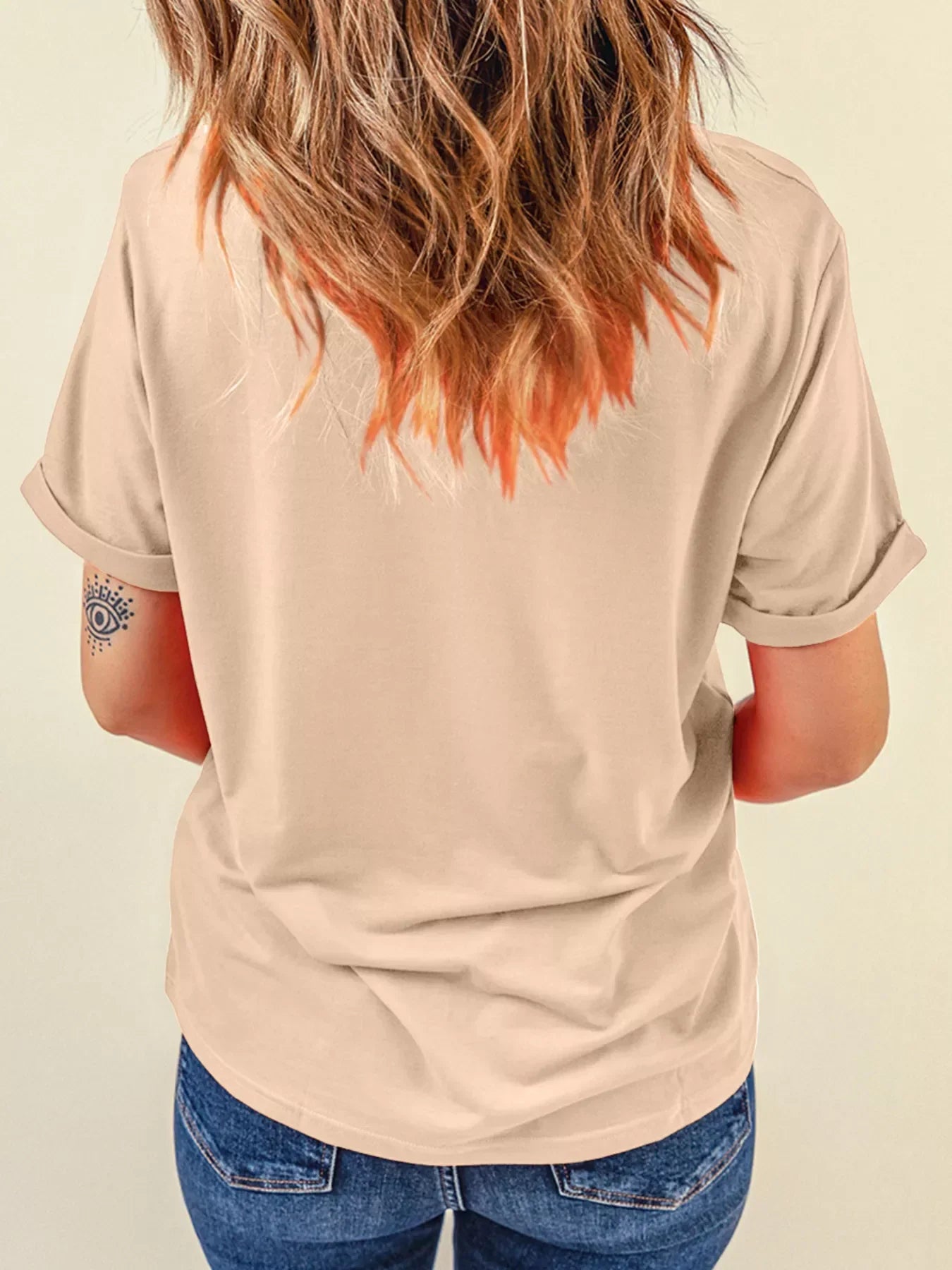Woman wearing beige short-sleeve t-shirt and blue jeans showing back with tattoo on arm