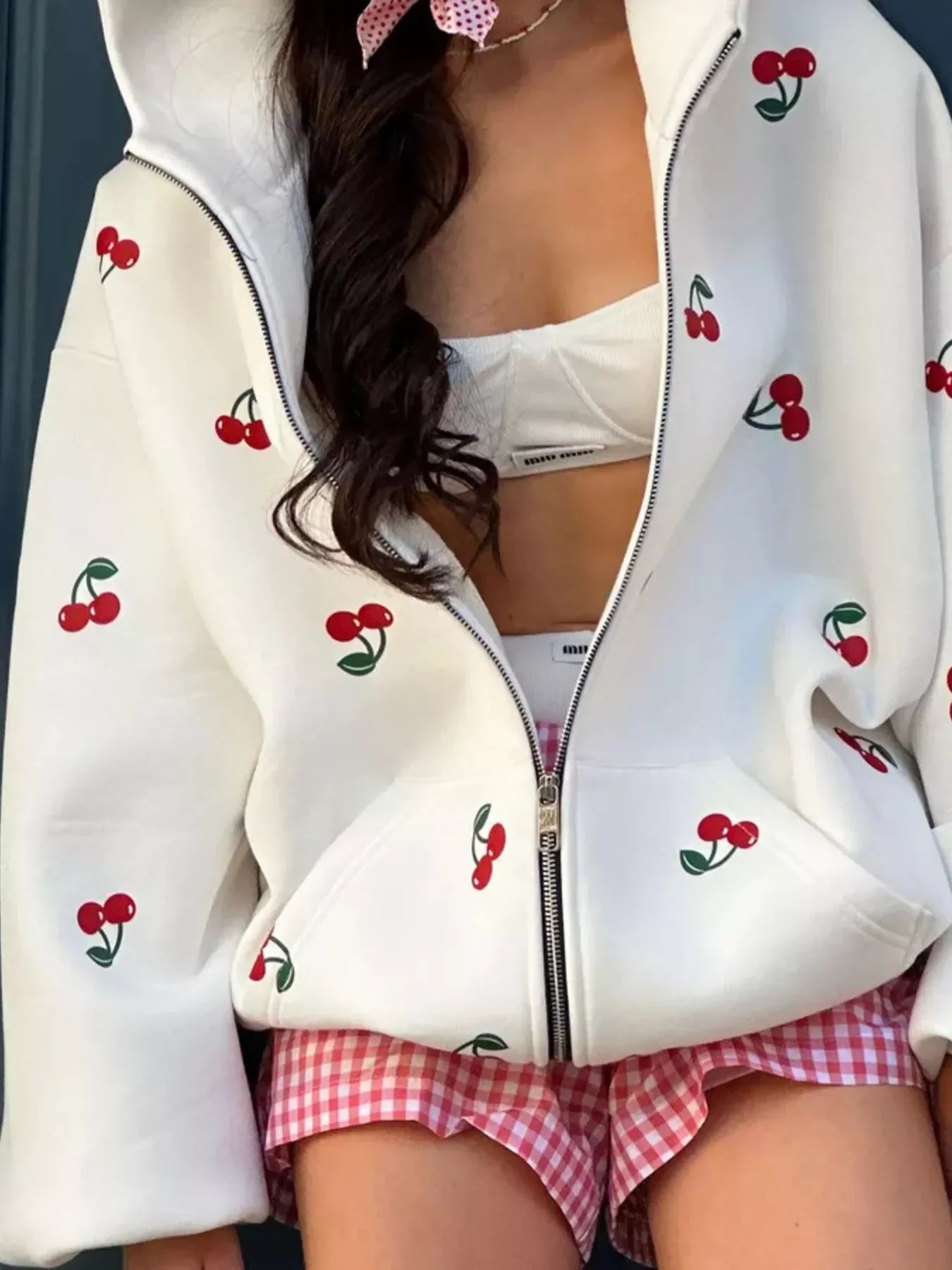 Woman wearing white cherry-print zip-up hoodie, white bralette, and pink gingham shorts